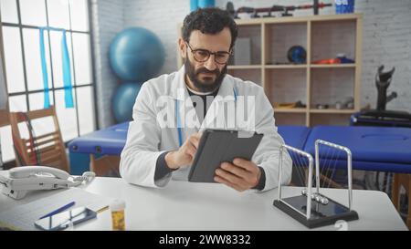 Middle-aged bearded man in lab coat using tablet at rehabilitation center clinic. Stock Photo