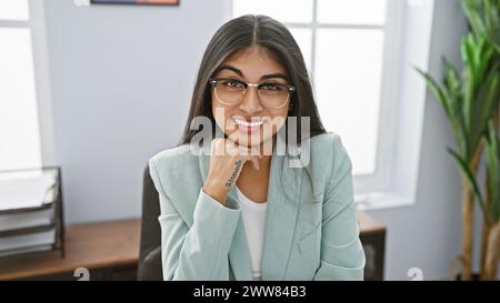 Smiling indian woman with glasses, long hair, in office wearing a light blue suit Stock Photo