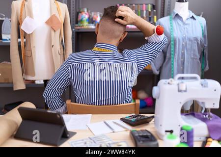 Hispanic man with beard dressmaker designer working at atelier backwards thinking about doubt with hand on head Stock Photo
