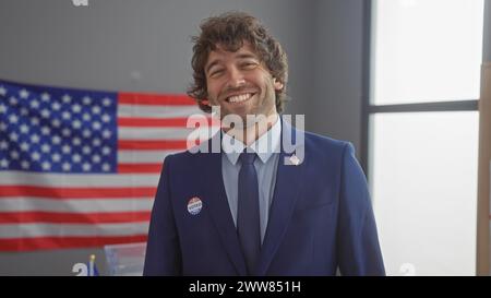 Young hispanic man smiling indoors with american flag background donning a suit and 'i voted' sticker Stock Photo