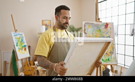 A focused hispanic man examines his painting in a bright art studio interior. Stock Photo