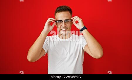 Handsome young hispanic man adjusting glasses against a vibrant red isolated background. Stock Photo
