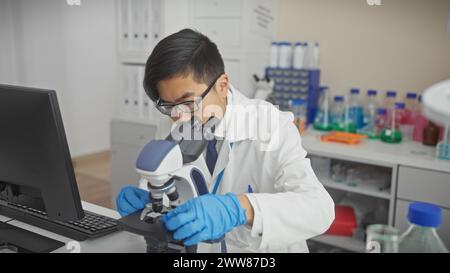 Asian man in lab coat using microscope in a modern laboratory indoors. Stock Photo