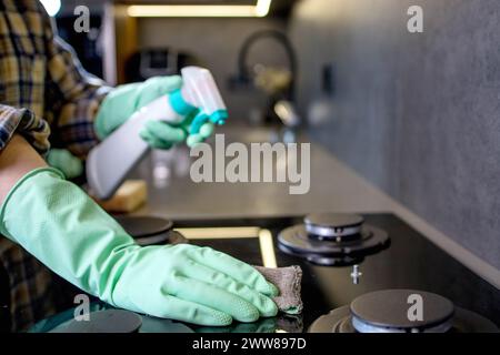 Hand in a green rubber glove washes the gas stove. Cleaning the kitchen. Stock Photo