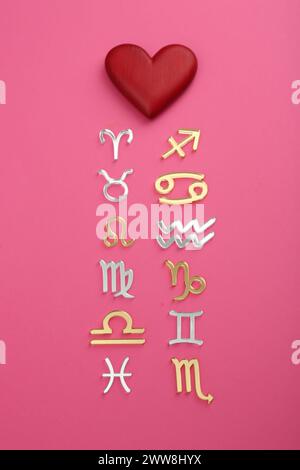 Zodiac compatibility. Signs with red heart on pink background, flat lay Stock Photo