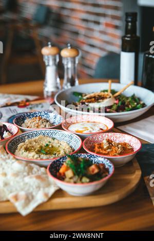 An assortment of Mediterranean mezze dishes served with fresh vegetables, hummus, and pita bread on a wooden board. Stock Photo