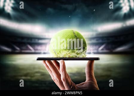 Tennis live online broadcast concept with hand holding a mobile phone with ball and tennis stadium in the background. Stock Photo