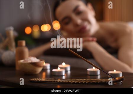 Spa therapy. Beautiful young woman lying on massage table in salon, focus on burning candles, salt and incense stick Stock Photo