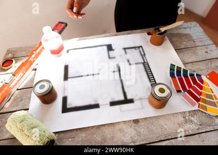 Plan of renovation of house on old wooden table. Top view. Sheet of paper with cans of paint and brushes, palette for choosing colors, construction le Stock Photo