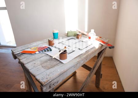 Plan of renovation of house on old wooden table. Top view. Sheet of paper with cans of paint and brushes, palette for choosing colors, construction le Stock Photo