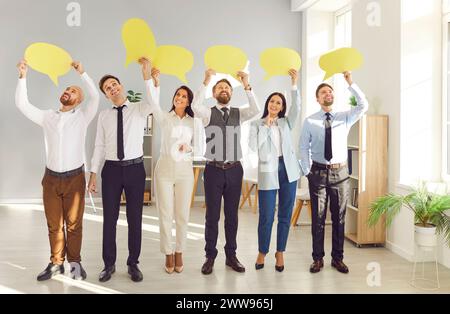 Young cheerful smiling business people employees holding yellow paper clouds standing in office Stock Photo