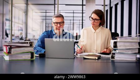 Two Businesspeople Calculating Invoice In Office While Using Laptop Stock Photo