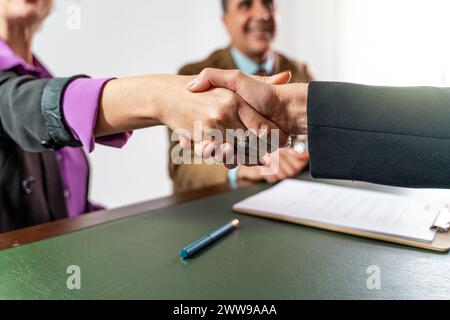 Two business professionals - engaging in a confident handshake over a signed legal document - success in negotiation, sealing a partnership agreement Stock Photo