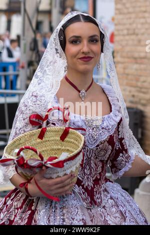 Burgundy Elegance at the Fallas; A woman in a traditional Fallera costume, adorned with lace and ribbons, holds the spirit of Gandia’s festival in her Stock Photo