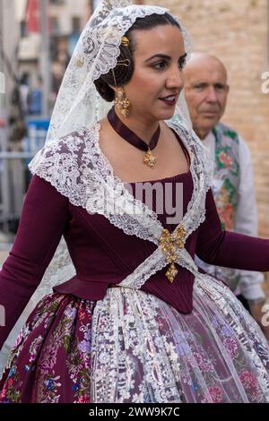 Valencian Festive Splendor; A Fallera’s golden attire glimmers against the celebration’s backdrop. Her burgundy dress, adorned with lace, captures the Stock Photo