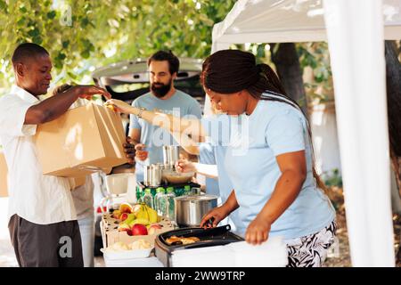 Generous volunteers distribute donations to individuals in need. Smiling charity workers provide meal boxes and packages to the homeless people and those experiencing poverty. Stock Photo