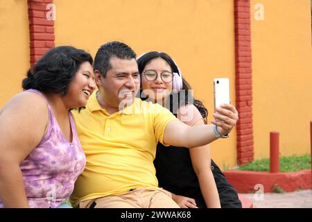 Divorced single dad with his dark-skinned Latino teenage daughters spending fun time using cell phone taking photos selfies Stock Photo