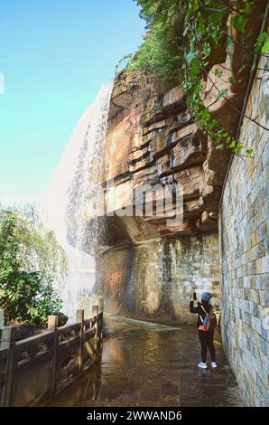 A tourist taking picture below the Kunming Waterfall curtain tunnel Stock Photo