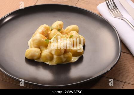 Delicious Italian gnocchi with white cheese sauce served on black plate placed on wooden table in restaurant Stock Photo