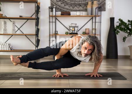 Focused adult male doing Eight Angle asana on mat while practicing fitness exercise at home Stock Photo