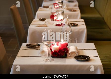 Row of tables decorated with burning candles and empty wineglasses on white tablecloth in luxury restaurant Stock Photo