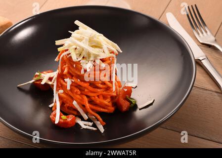 Appetizing spaghetti pasta with tomato sauce and parmesan served on black plate on wooden table in restaurant Stock Photo