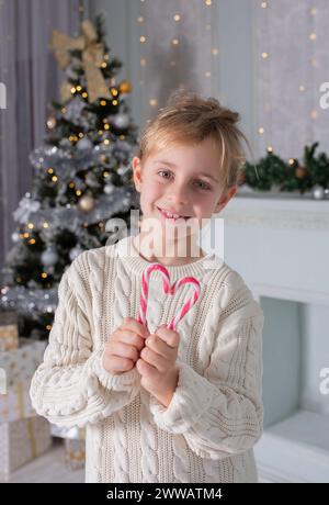 Christmas Candy Heart. New Year's little girl put together heart-shaped Christmas caramels. Christmas portrait in brihgt background Stock Photo