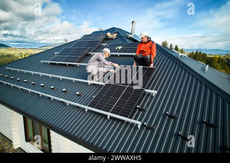 Male technicians adjusting the solar panel on roof of house. Solar system installation on top of building. Engineers in helmets installing solar panel system. Stock Photo