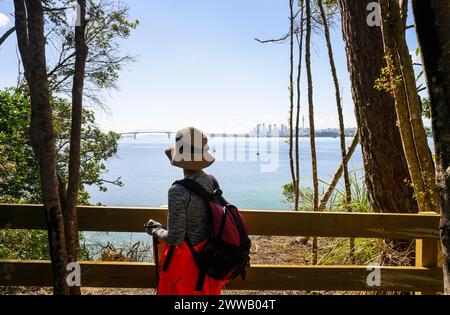 Woman enjoying the view of Auckland Harbour Bridge and Sky Tower from Kauri Point Centennial loop track. Auckland. Stock Photo
