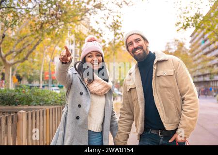 Happy friends or couple walking, pointing at smart hotel location outdoors. Stock Photo