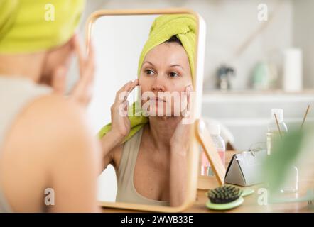 Middle-aged woman examining her facial skin looking in the mirror put on the table Stock Photo