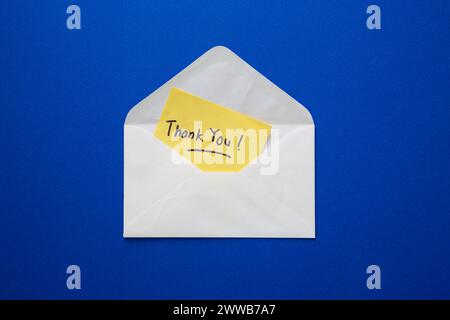 Yellow sticky note with thank you! text inside an open white envelope on blue background Stock Photo