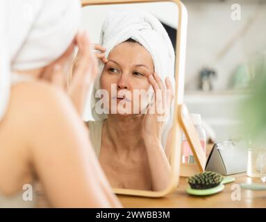 Middle-aged woman examining her facial skin looking in the mirror put on the table Stock Photo