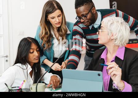A diverse group of professionals engaged in a collaborative discussion with digital devices - interaction and technology - multicultural office enviro Stock Photo
