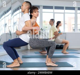 Group of men and women doing acroyoga exercises in pairs, exercising partner yoga during training in fitness center Stock Photo
