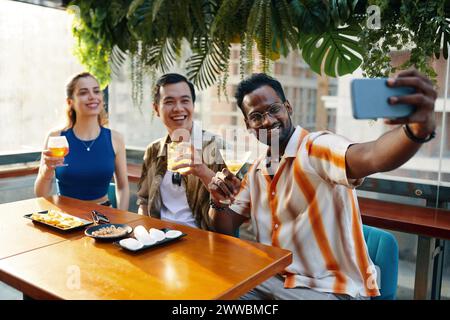 Excited man taking selfie with friends when sitting at table in bar Stock Photo