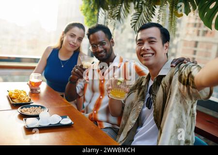 Smiling Vietnamese man taking selfie with best friends in bar Stock Photo