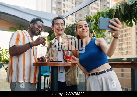 Smiling young woman taking selfie with colleagues when they are resting in bar Stock Photo