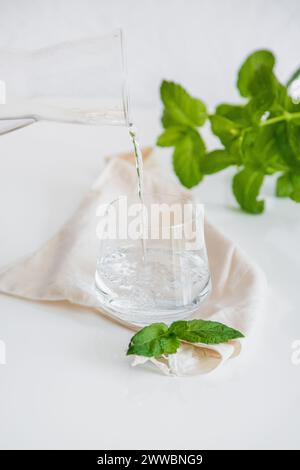 Person taking a jug of water to pour with a glass. Glass cup containing natural water on white background. Minimalist image. Drinking water simplicity Stock Photo