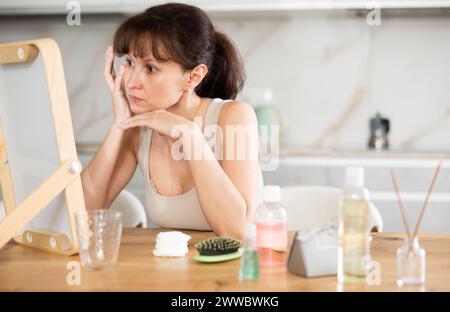 Middle-aged woman examining her facial skin looking in the mirror put on the table Stock Photo