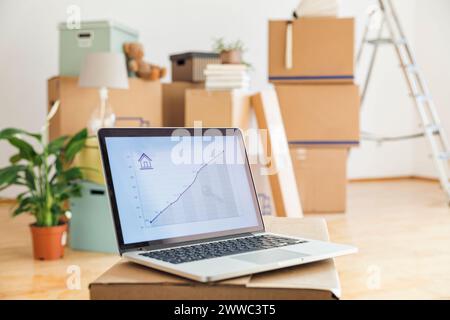 Rising line graph on laptop screen in front of cardboard boxes in an empty room in a new home Stock Photo