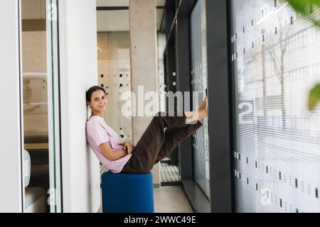 Smiling young businesswoman sitting in office corridor Stock Photo