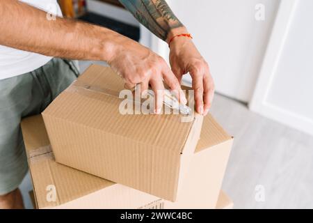 Hands of man opening cardboard box with utility knife at new home Stock Photo
