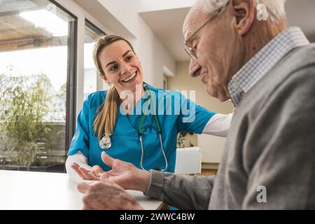 Smiling nurse taking pulse of senior man sitting at table Stock Photo