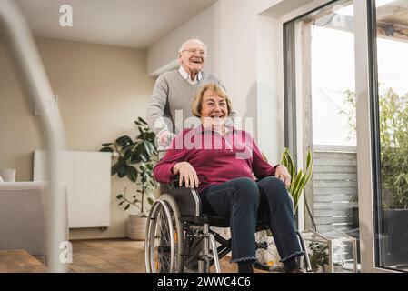 Happy man with woman sitting in wheelchair at home Stock Photo