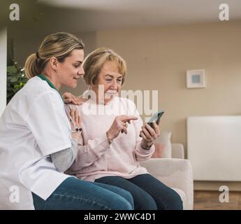 Smiling doctor with senior woman using smart phone at home Stock Photo