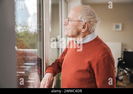 Thoughtful senior man looking through window Stock Photo