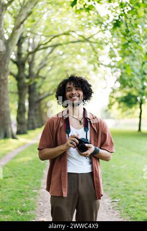Smiling man holding camera and standing at park Stock Photo