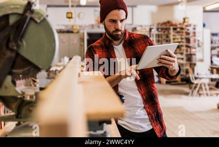 Young carpenter using tablet PC by machinery at workshop Stock Photo