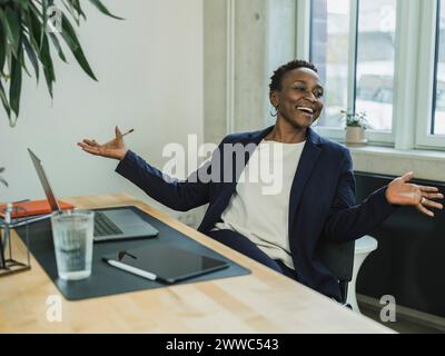 Happy businesswoman gesturing sitting at desk in office Stock Photo